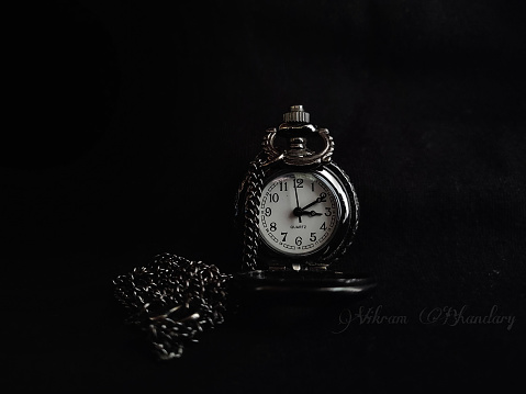 Antique pocket watch from 1917 with an old U.S silver dollar on black background.