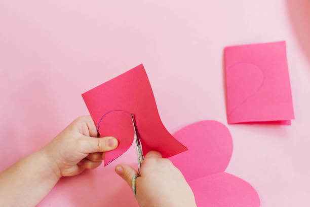 istock Step by step instructions. How to make a paper heart card for Valentine's Day. Creative crafts. Do it yourself. Child cuts a heart out of paper, makes a card with her own hands 1366245233