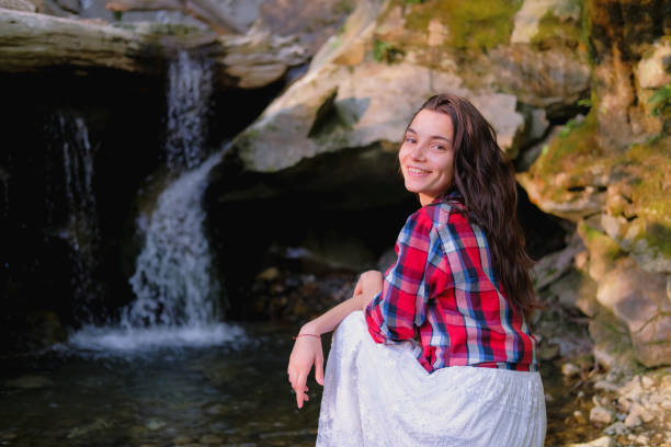 junge frau in weißem kleid und kariertem hemd genießt einheit mit der natur im freien vor dem hintergrund des wasserfalls. - waterfall water nature zen like stock-fotos und bilder