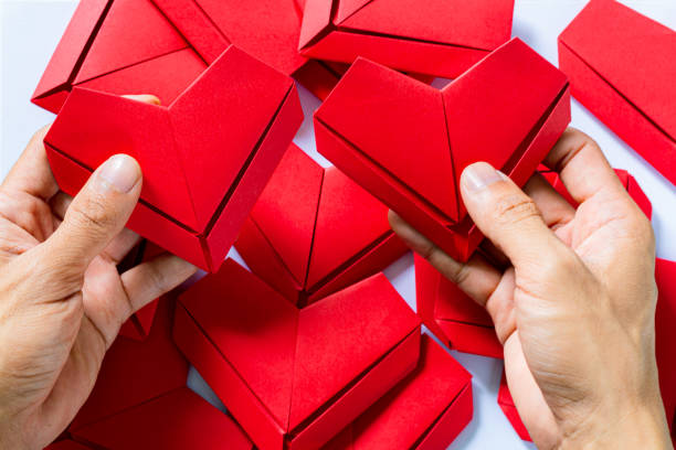 corazón de papel, manos que sostienen el fondo blanco del corazón de origami doblado, la mano del niño que sostiene el papel del corazón rojo sobre fondo azul - possing love passion romance fotografías e imágenes de stock