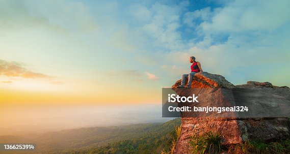 istock man on the cliff,Young man tourist with backpack relaxing on top rock and enjoying sunset,Young Man sit on the peak of great rock. 1366253914