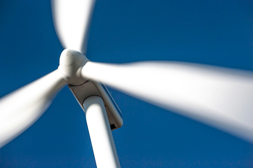 White rotor blades of a wind turbine against a blue sky background blurred by the motion blur