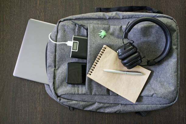 istock Modern laptop backpack lies with an external battery, smartphone, notepad, pen, silver laptop and headphones on a wooden table. Travel, trip and learning concept with gadgets in a backpack 1366260499