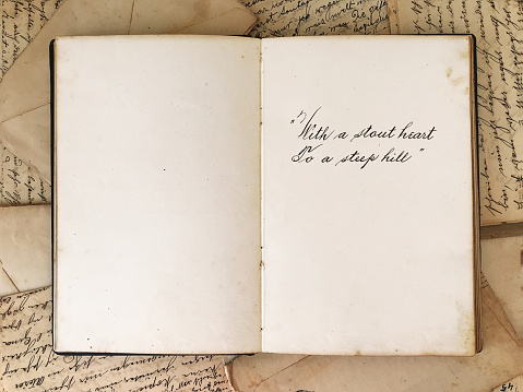 Overhead view of a vintage journal open-wide with a calligraphy dedication on one of its pages,  on top of old scattered letters from the beginning of the 20th century.