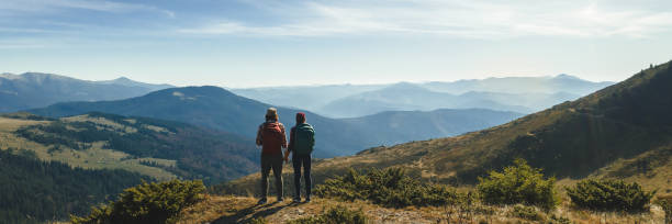 Couple of Hikers With Backpacks in Front of Landscape Valley View on Top of a Mountain stock photo