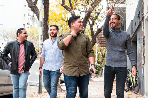 group of friends talking and smiling to each other and walking towards a bar on the sidewalk of an argentinian street on an autumn day. lifestyle concept.