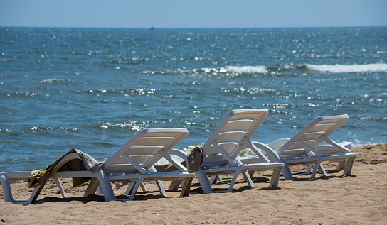 The seashore without people on a sunny summer vacation day. A white plastic sunbed stands on the white sand beach against the background of the sky and sea waves.