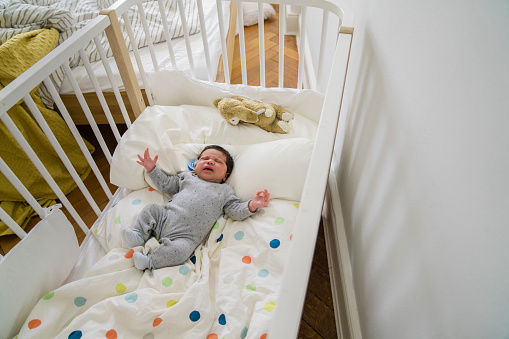 Top view of a cute little baby boy crying in baby crib in bedroom. Newborn child in crib at home.
