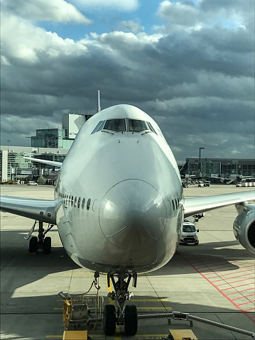 Font of a modern airplane parked in an airport. Close-up wide angle shot with heavy clouds.