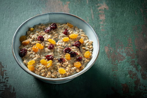 Overnight oats vegan recipe breakfast bowl homemade, including ingredients as rolled oats, soy milk, peanut butter, ground flaxseed, banana, maple syrup dried cranberries and raisins.