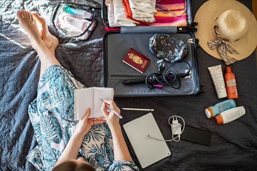 Young woman doing her last check to be sure if she have everything she needs for vacation while packing stuff in bedroom