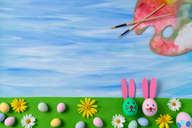 Painting Easter eggs with easter bunny brushes and palette on blue watercolor background with daisy spring flowers