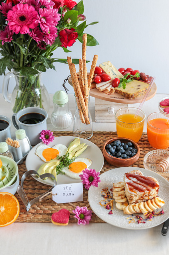 Homemade breakfast brunch table for mother’s day with flower bouquet, eggs, pancakes and fresh juices