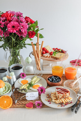 Homemade breakfast brunch table for mother’s day with flower bouquet, eggs, pancakes and fresh juices