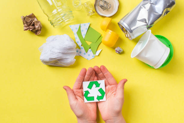 Recycle sign in child hands, clean trash metal, plastic paper and glass. Recycling concept on yellow stock photo