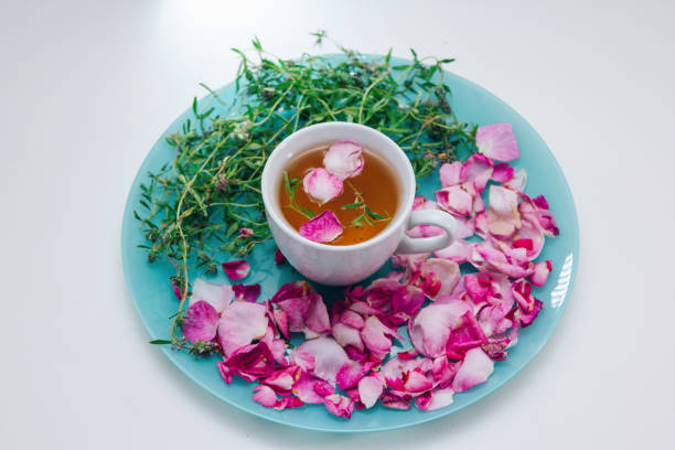 Homemade herbal tea in a white cup. Tea rose petals and thyme on a plate -ingredients for hot healthy drink