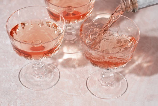 vin mousseux rose ou champagne versé de la bouteille dans des verres en cristal sur fond de marbre rose. composition créative minimale avec espace de copie. - champagne pouring champagne flute glass photos et images de collection