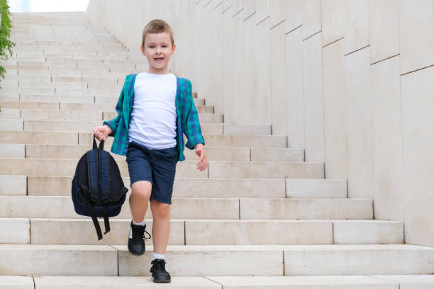Schoolboy with a backpack in his hand on the street on the way to school goes down the stairs. Back to school.