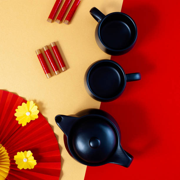 istock Chinese New Year red and gold background composition with teapot, teacups, firecrackers and red paper fan with yellow flowers. 1366290557