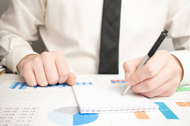istock Business analyst working - hand with pen, calculator, coffee, magnifier, worksheet and graph 1366297454