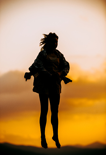 Full length of a sporty silhouette young woman jumping over sunset sky