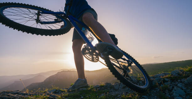 istock Strong fit male mountain biker performing stunts on rocky terrain on a sunset while wearing a blue shirt and riding a blue bike 1366299080