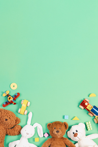 Baby kids toys background. Teddy bears, wooden train, toy cars, colorful blocks on light green background