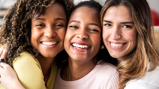 Three beautiful smiling girl friends hugging together - Multiracial group of women looking at camera - Females and happy lifestyle concept