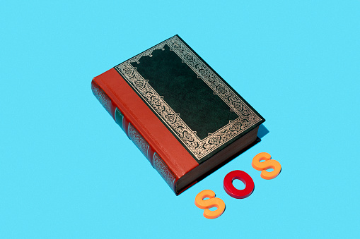 Book next to colored plastic letters writing the abbreviation of the word SOS on a blue background.