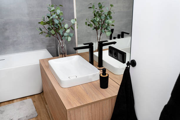 nowoczesna umywalka w łazience w szafce naściennej z matowym czarnym kranem, widocznym lustrem i sztucznymi kwiatami. - bathroom black faucet zdjęcia i obrazy z banku zdjęć