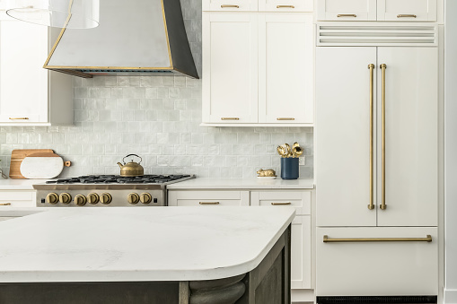 Elegant Kitchen Design with white matte refrigerator, white cabinets, and two toned kitchen island. Gray tile backsplash and metal range hood.