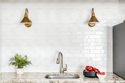 Kitchen counter and sink with marble countertops and white subway tile backsplash with gold light fixtures.