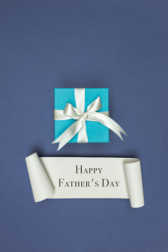 Blue gift box with white ribbon on blue background and white card with Happy Father’s day text.