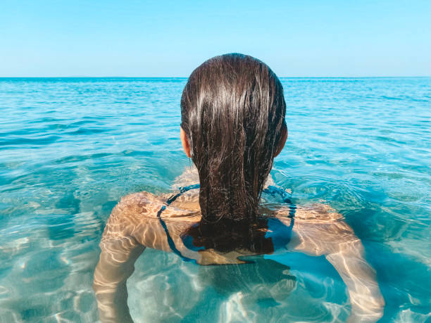 Backview of Woman in Sea Back view of caucasian woman with long hair in sea wearing a black swimsuit. waist deep in water stock pictures, royalty-free photos & images