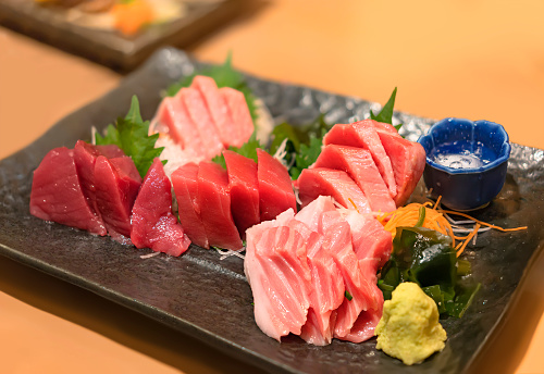 Healthy Japanese fish dish of an assortment of sliced pieces of tuna maguro sashimi served with wasabi mustard, wakame seaweed and shiso leaves in a plate.