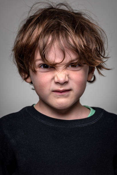 Very upset caucasian little boy looking at the camera on gray background