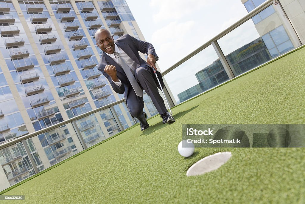 Empresário afro-americano jogando golfe em arranha-céu na cobertura - Foto de stock de Golfe royalty-free