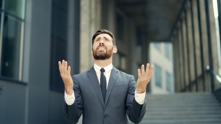 Portrait young bearded businessman begs God for success With Hope raising his hands up to sky