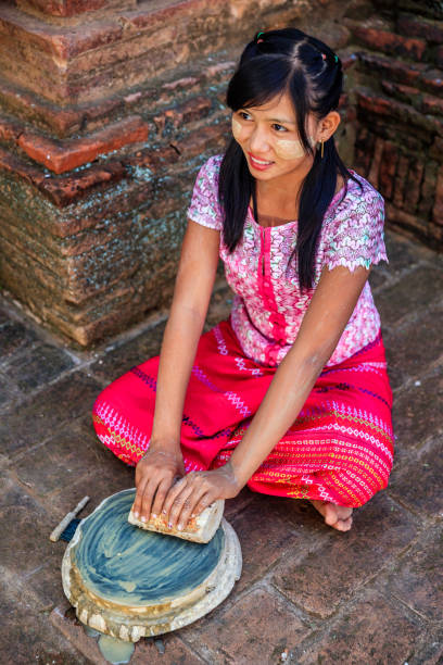 Young Burmese girl with thanaka face paint preparing thanaka paste in the ancient temple of Bagan, Myanmar (Burma). Thanaka is a yellowish-white cosmetic paste. Thanaka  gives a cooling sensation and provides protection from sunburn.