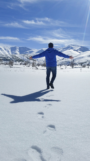 A man with blue jacket embracing snowy nature and having joy and being happiness