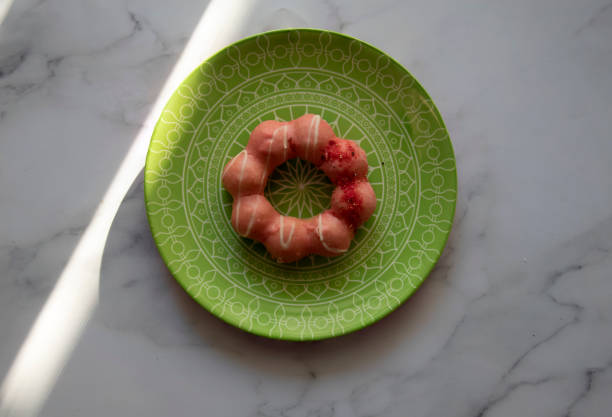 Pink strawberry  glazed Mochi Donut with sprinkles, on a green plate with a geometric pattern.