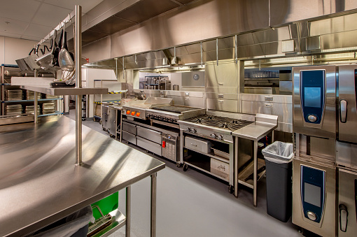 Young professional cook in uniform wiping kitchen counter in kitchen after cooking