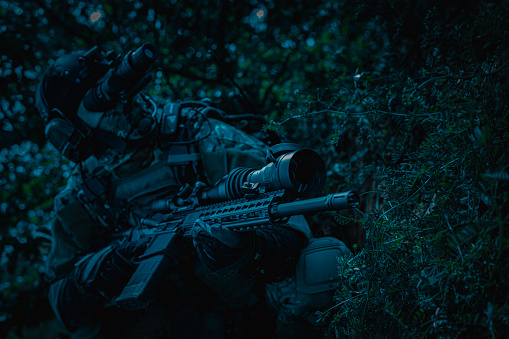 A soldier with a weapon in his hands and a night vision device. Armed man at night in the forest.