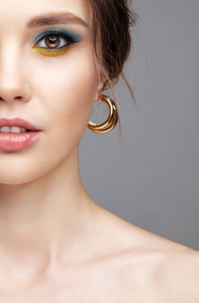 Portrait of young woman on gray background. Portrait of young woman on gray background. Female half face. with a ring in the ear. Makeup with blue eyeshadow and yellow eyeliner. gold earring photos stock pictures, royalty-free photos & images