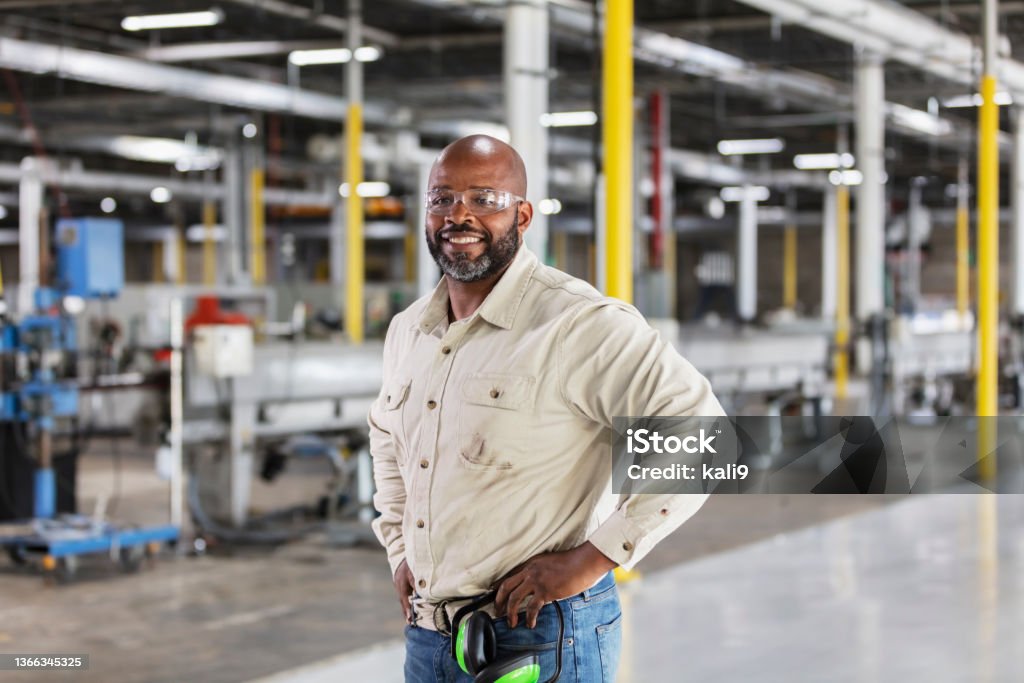 African-American man working in plastics factory A mature African-American man working in a plastics factory. He is standing on the factory floor with his hands on his hips, smiling at the camera. Manufacturing Stock Photo