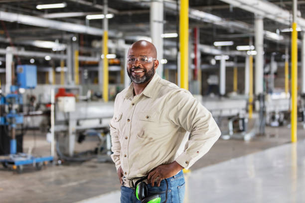 African-American man working in plastics factory A mature African-American man working in a plastics factory. He is standing on the factory floor with his hands on his hips, smiling at the camera. working class stock pictures, royalty-free photos & images