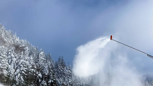 Snow cannon. Snowmaker in action at ski resort, spraying artificial snow with snow covered forest in the background.