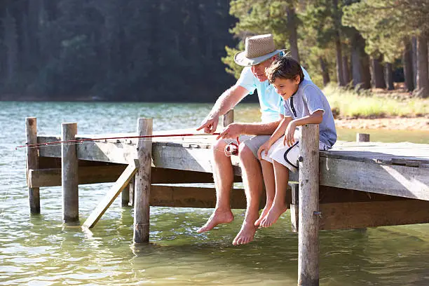 Senior man sitting on jetty fishing in lake with grandson
