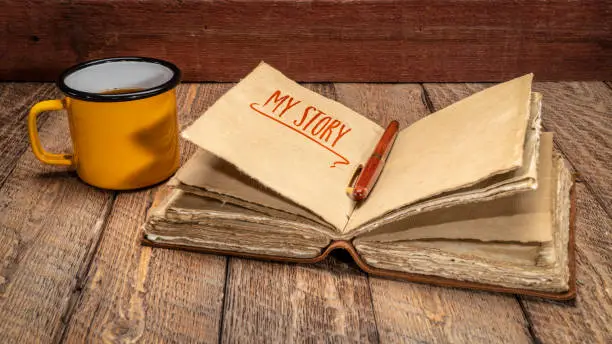 my story - handwriting in a retro  leather-bound journal with decked edge handmade paper pages and cup of tea on rustic wood, journaling concept