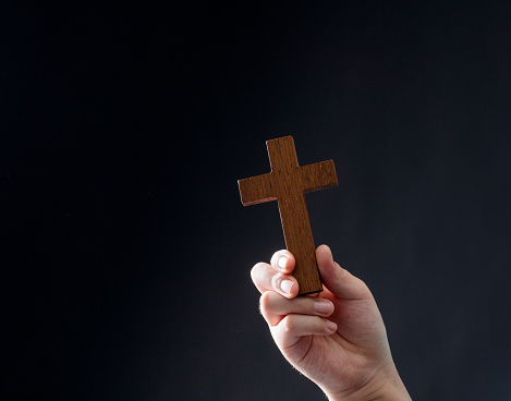 Human hand holding religious cross on black background.
